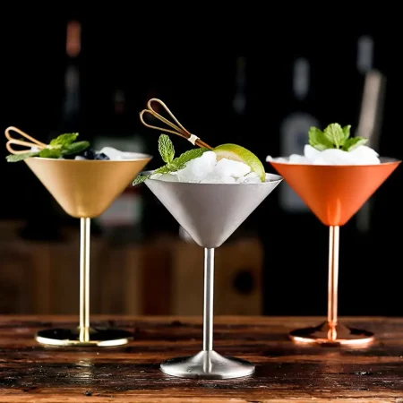 A collection of three metallic martini glasses in gold, silver, and copper finishes, made from food-grade stainless steel, each filled with ice and garnished with lime and mint.