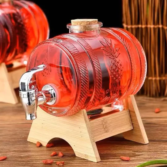 A transparent, red-tinted glass beverage dispenser with a pineapple design, mounted on a wooden stand with a tap at the front.