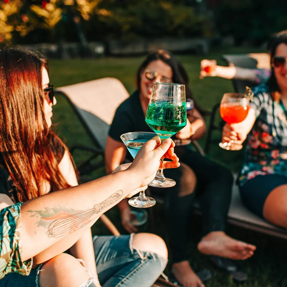 Two hands holding glasses with colorful beverages at an outdoor gathering, highlighting the elegance and versatility of premium drinkware for both casual and formal events.