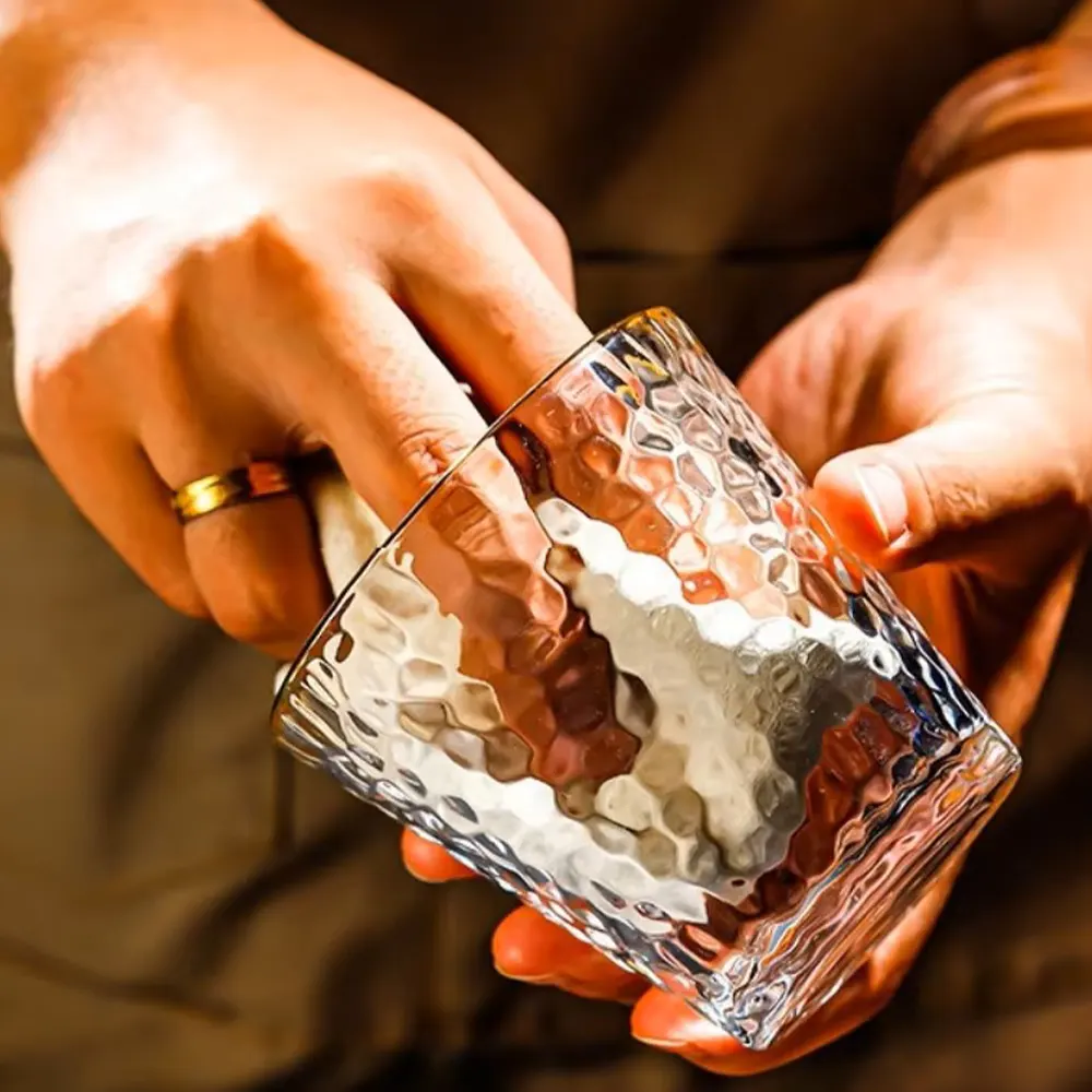 Close-up of two hands holding a Golden Cascade Tumbler with a hammered glass texture and gold rim, emphasizing the elegant design and comfortable grip.”