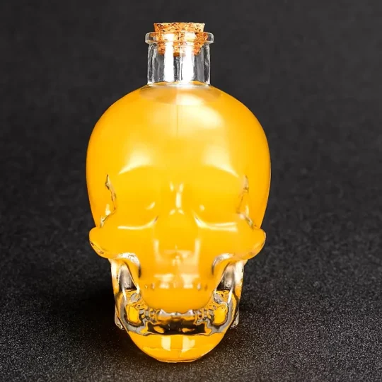 Clear glass skull-shaped Grim Reaper Bottle filled with yellow liquid, featuring detailed facial features and a cork stopper, perfect for storing spirits and themed events.