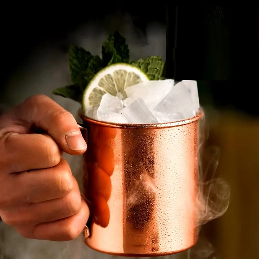 Person holding a copper-plated stainless steel Moscow Mule mug with ice, lime slice, mint leaves, and condensation.