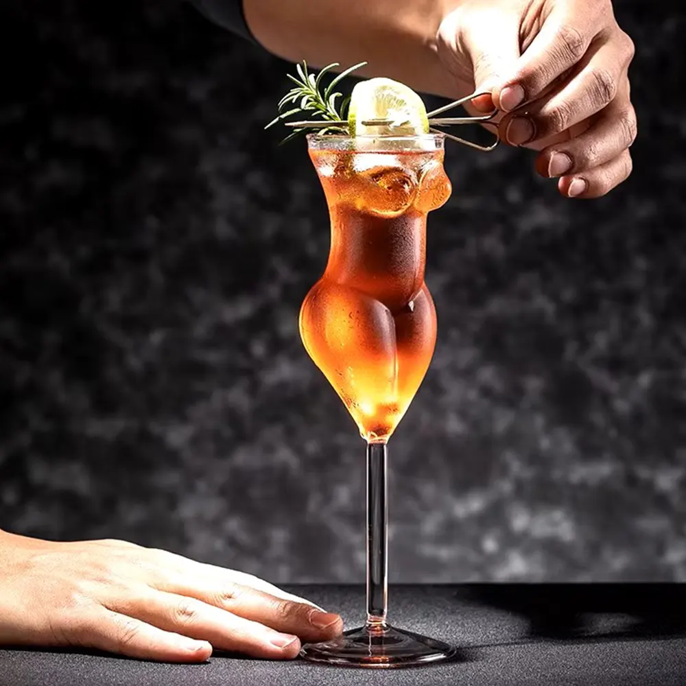 Hand holding a 200ml La Belle Femme stemmed glass with a woman’s silhouette, filled with a dark cocktail, garnished with rosemary and lemon, set against a dark background.