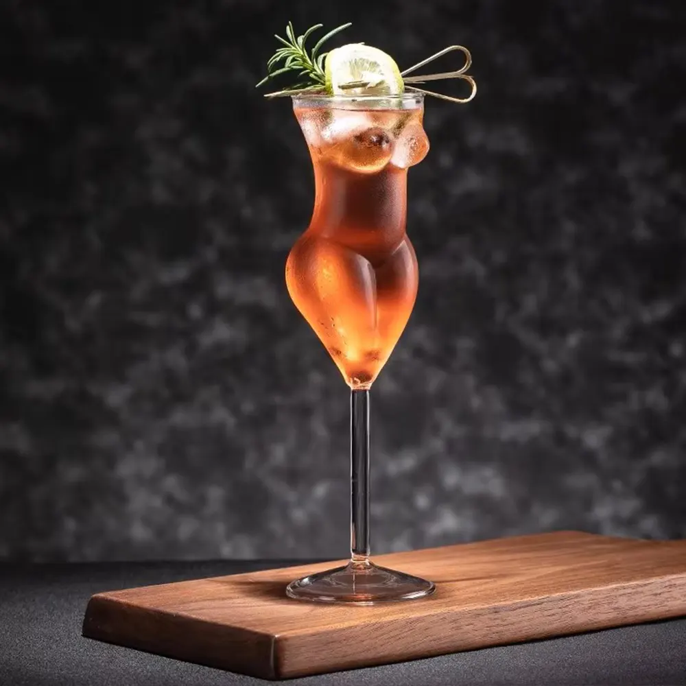 200ml La Belle Femme stemmed glass with a woman’s silhouette, filled with a dark amber cocktail, garnished with rosemary and lime, set on a wooden surface against a dark background.