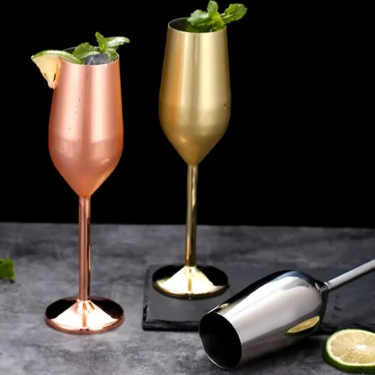 Three stainless steel champagne glasses in silver, gold, and copper finishes, each holding 200 ml, displayed on a dark surface with a gray background.