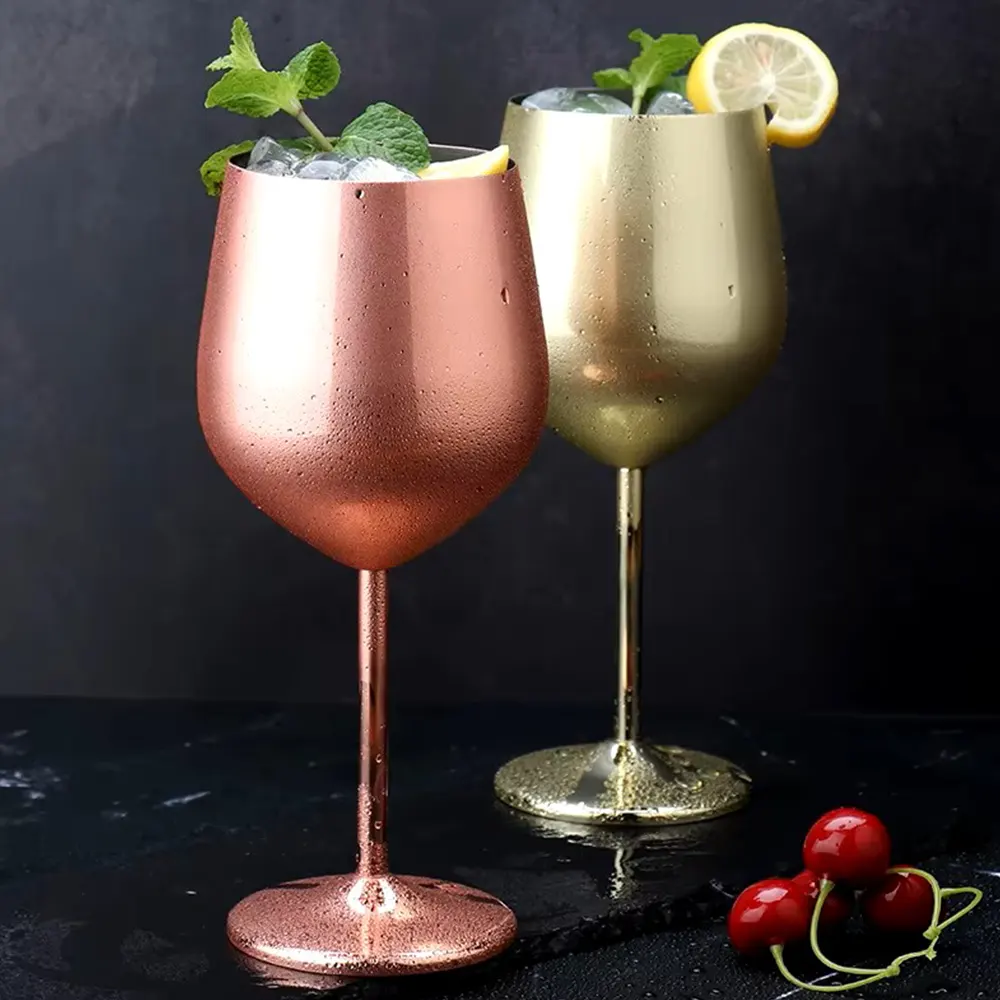 Close-up of silver and copper metallic wine glasses with a smooth finish, filled with ice and garnished with mint leaves and lemon slices, set against a dark background.