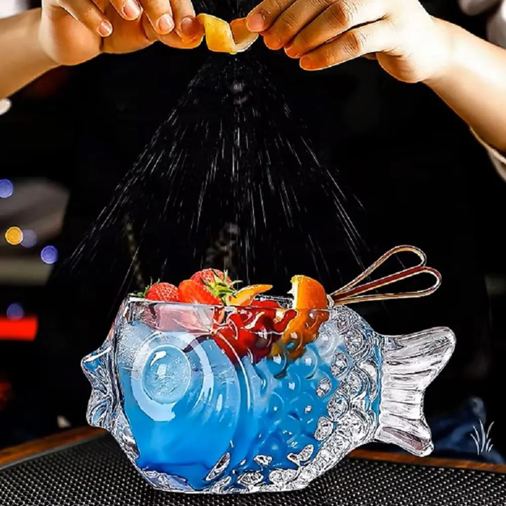 A fish-shaped cocktail glass named Mr. Fishy, filled with blue liquid, garnished with strawberries and a lemon slice, with a person squeezing lemon juice into the glass.