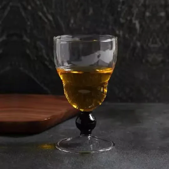 A close-up of the Obsidian Sphere 5 oz Whisky Glass featuring an elongated shape and a distinctive black-beaded stem, placed on a dark stone countertop.