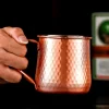 Close-up of a hand holding a hammered texture copper-plated stainless steel Moscow Mule mug, 500 ml capacity.