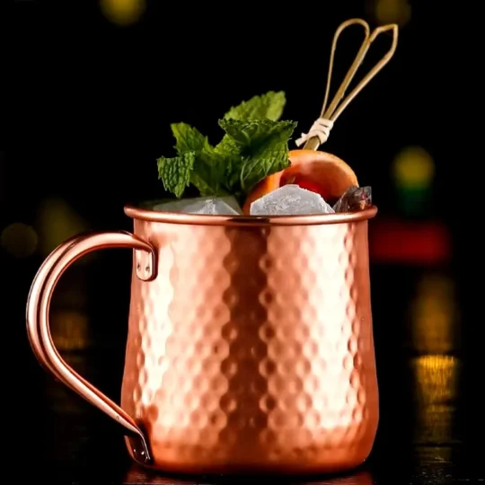 Hammered texture copper-plated stainless steel Moscow Mule mug with ice, mint, lime garnish, and cocktail stirrer, 500 ml capacity.