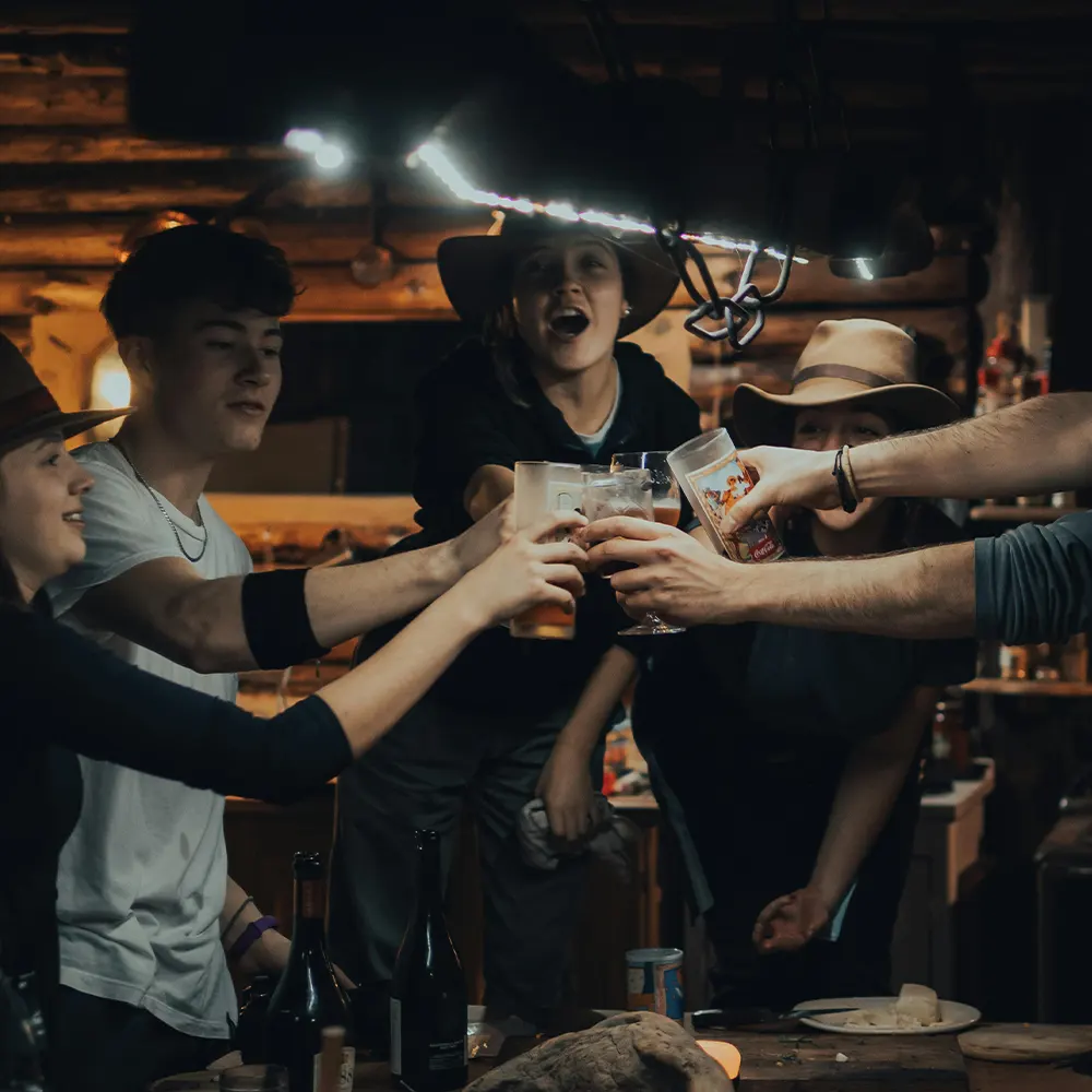 A group of individuals toasting with various glasses in a cozy, rustic indoor setting, highlighting the whimsical design of premium drinkware perfect for gatherings like Halloween parties, Thanksgiving dinners, and casual get-togethers.