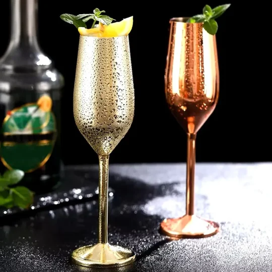 Two stainless steel champagne glasses, one in gold and the other in copper finish, each holding 200 ml and garnished with mint leaves and a citrus slice.