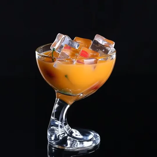 Clear cocktail glass with a unique spiral design, filled with yellow-orange liquid, ice cubes, and fruit bits, perfect for cocktails.