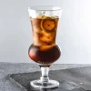 A 660 ml round belly cocktail glass filled with a dark-colored iced beverage, garnished with a slice of lemon, placed on a grey stone surface.