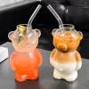 Two bear-shaped cocktail glasses, ‘The Honey Bear,’ one filled with a pink drink and lime slice, the other with a gradient drink from white to brown, both with metal straws, placed on a counter.