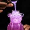 Close-up of ‘The Honey Bear’ cocktail glass being filled with a bubbling purple liquid from a metal ladle, highlighting the bear-shaped design and dynamic motion of the pour.