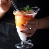 A person holding an eco-friendly cocktail glass with a spiral pattern, filled with a layered frozen dessert in orange and white, topped with mint.