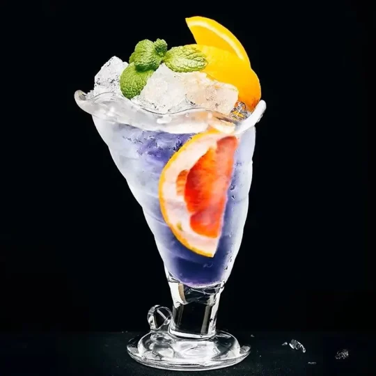 A colorful beverage with a gradient from purple to clear, garnished with orange slices, mint, and grapefruit, in an eco-friendly cocktail glass with a spiral pattern.