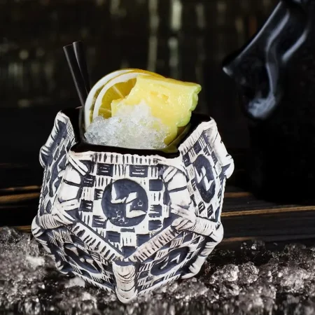 Close-up of a ceramic tiki mug named Aloha Sipster with black and white tribal patterns, filled with a cocktail garnished with lemon slice and crushed ice.