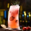 500 ml Vertical Elegance tall glass with unique hunched design and vertical ridges, filled with a pink cocktail, garnished with rosemary, citrus slice, and red berries.