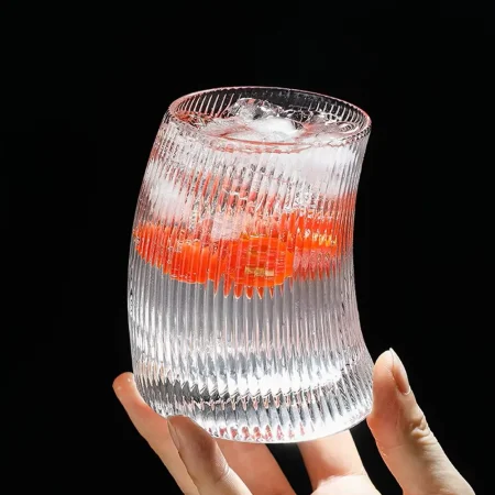 Hand holding a 340 ml Vertical Elegance glass with unique hunched design and vertical ridges, filled with a layered cocktail and ice cubes