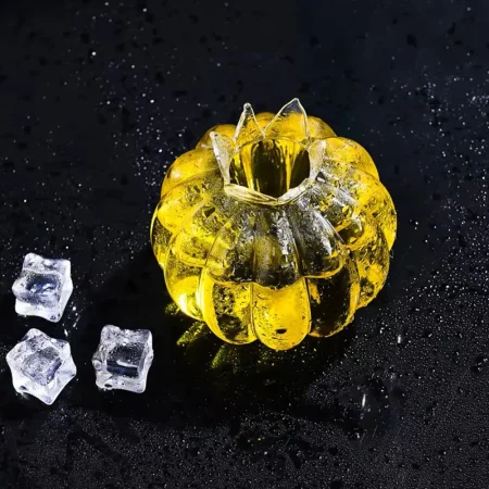 Hand-blown Pumpkin Twist Glass made from heat-resistant borosilicate, featuring a translucent yellow pumpkin design, surrounded by ice cubes on a dark background.