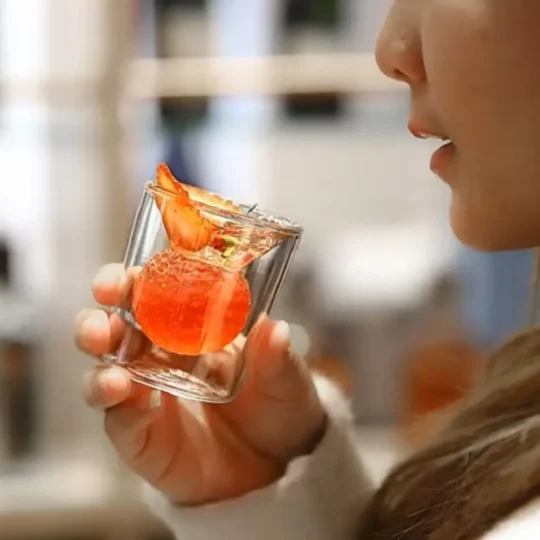 A Dual Illusion Tumbler held in a hand, containing a layered cocktail