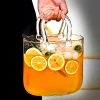 Hand holding the ‘Sip ‘n’ Carry’ cocktail glass, an innovative handbag-shaped drinkware filled with citrusy cocktail, lemon slices, and mint garnish.