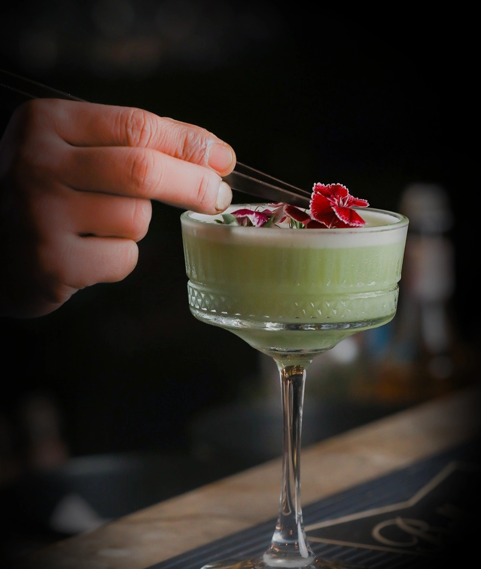 Hand holding the regal tweezer from the imperial collection and using it to place garnish on a carved coupe glass filled with a green cocktail